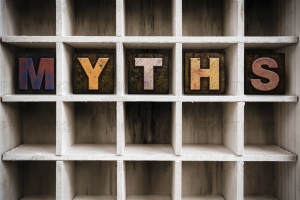 The word MYTHS written in vintage ink stained wooden letterpress type in a partitioned printer's drawer