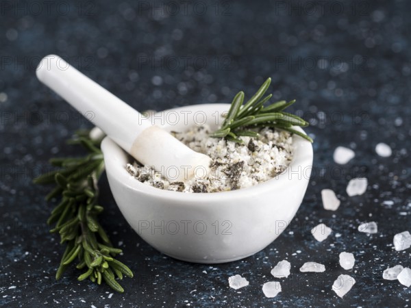 Close up view of mortar and pestle with sea salt scented rosemary and lemon zest. Sea salt scented herb rosemary on dark blue background. Scented salt and ingerdients. Copy space