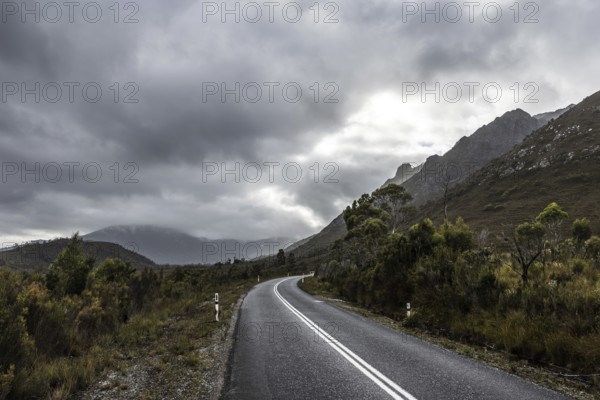 The picturesque Gordon River Rd at the Sentinel range of mountains near Bitumen Bones Sculpture on a cool wet summer's morning in Southwest National Park, Tasmania, Australia, Oceania