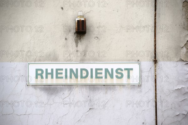 A close-up of a warning light with a rusty siren and a sign on the wall of an industrial ruin