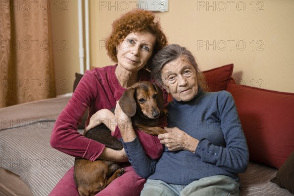 The theme is animal therapy, caring for elderly with dementia and Alzheimer's disease. Adult women spend time with elderly mother and pets dogs to bring joy and pleasure, affection for loved ones