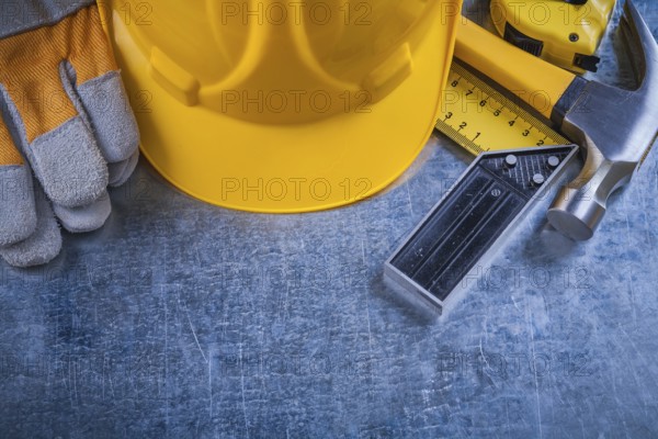 Square ruler safety gloves tape-measure building helmet and claw hammer on scratched metallic surface construction concept