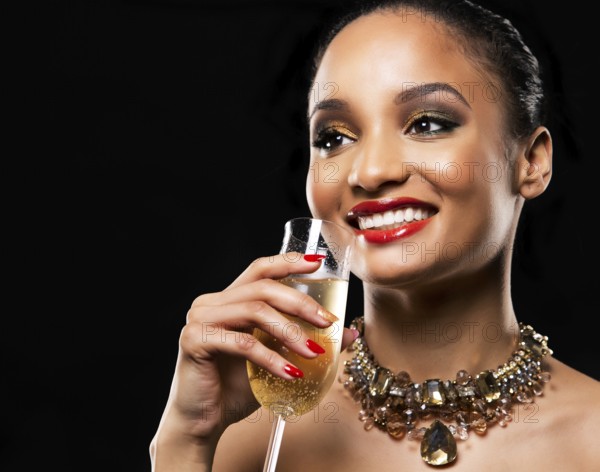 Romantic Indian woman with golden makeup and nailpolish. Big gold fashion necklace. Black isolated background. Holding glass of champagne, Toronto, Canada, North America