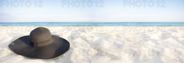 Banner Black hat on a background of the sea. Beach accessory on white sand. Straw panama on the background of the ocean