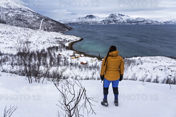 A woman in winter clothing stands above the small bay of Skjellvika on the island of Kvaloya, Tromso, Troms, Norway, Europe