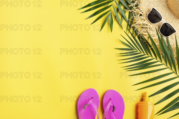 Vacation travel planning simple theme of straw hat sunglasses flip flops and palm leaves on uniform yellow background flat lay with copy-space