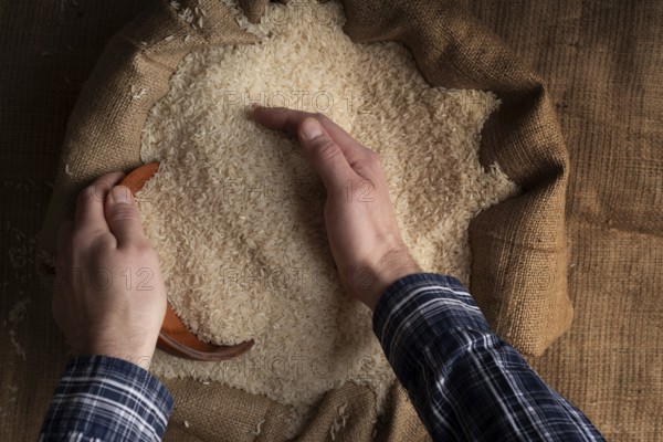 Human hands holding handful of rice over burlap sack