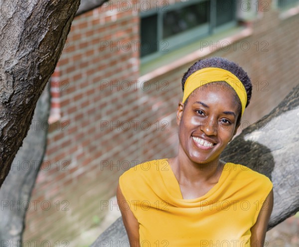 Smiling woman in a yellow dress with a headband, standing near a tree and brick wall, Taken in Daejeon, South Korea, Asia
