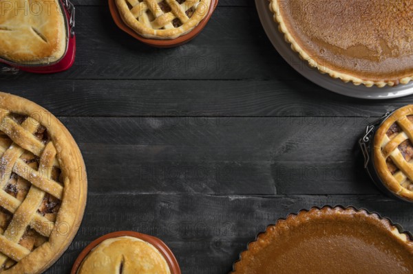 Kitchen table full of different pies, pumpkin pies, apple pies, with empty space in the middle. Traditional holidays dessert. Sweet pastry baking