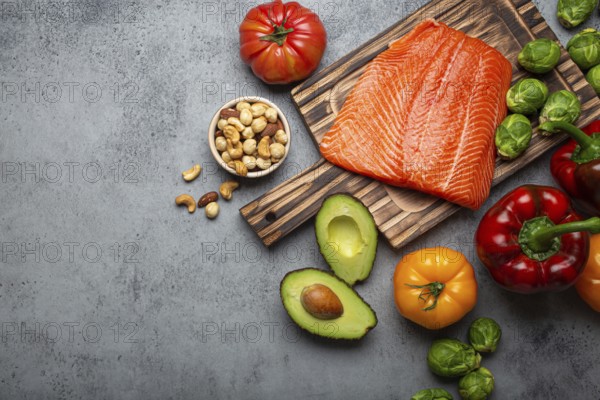 Fresh raw salmon fillet on wooden cutting board, organic bio vegetables and nuts on rustic stone grey background top view. Ingredients full of vitamins for healthy diet and nutrition, space for text, food photography, food photography