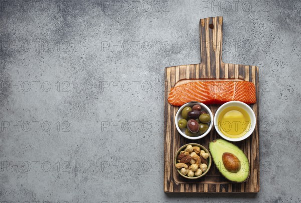 Food sources of healthy unsaturated fat and omega 3: fresh raw salmon fillet, avocado, olives, nuts on cutting board, rustic stone background top view. Healthy nutrition and keto diet, space for text, food photography, food photography