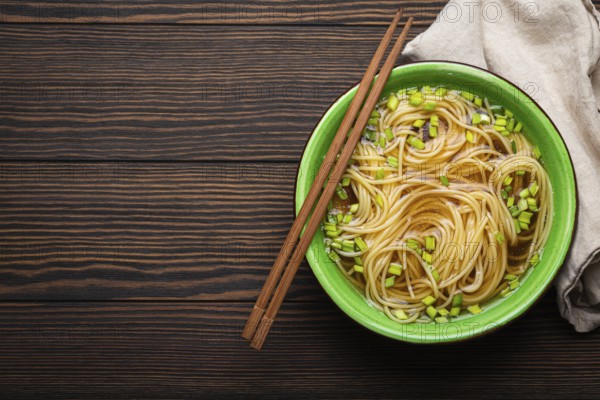 Asian noodles soup in green rustic ceramic bowl with wooden chopsticks top view on dark wooden background. Lo mein noodles with bouillon and green onion, space for text, food photography, food photography