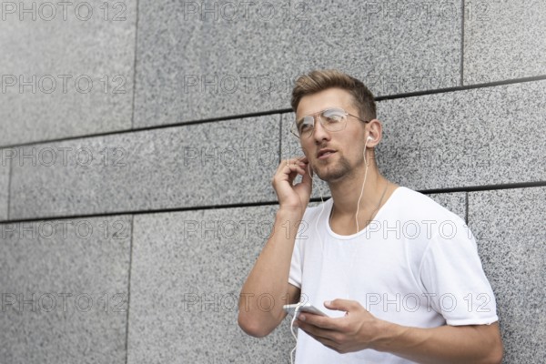 Earphones concept. People, technology, travel and tourism, man with earphones, smartphone on city street and listening to music over gray wall background
