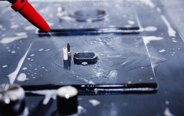 Close-up of a red nozzle spraying water onto a soapy stove surface