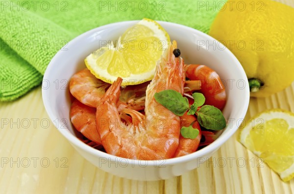 Raw shrimp in a white bowl with lemon, basil and green cloth on a wooden board