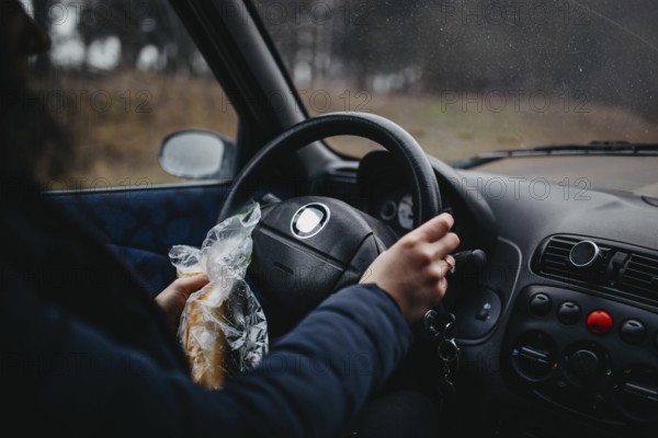 Person holding a sandwich and steering wheel in a car, capturing a casual driving moment