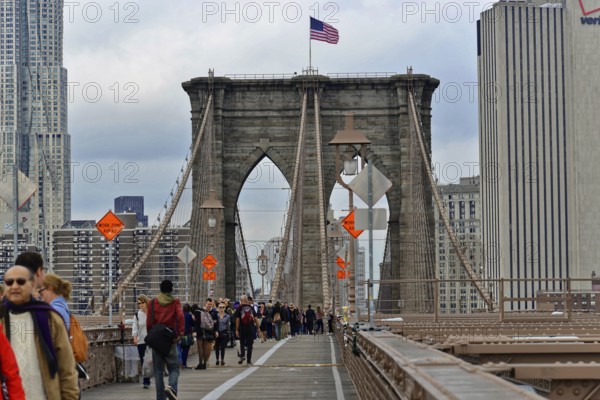 Brooklyn Bridge in Brooklyn, Manhattan, New York, USA United States of America, Pedestrians on the Brooklyn Bridge with urban scenery and a flag, New York City, USA, North America