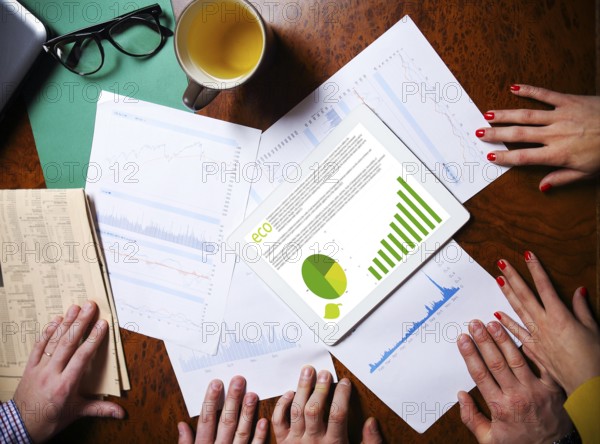 Business team hands at work with financial reports and a tablet computer, top view