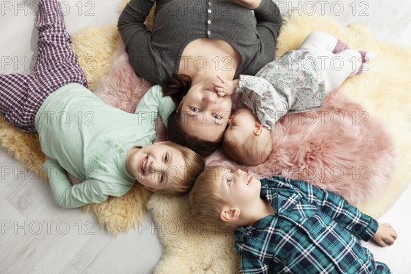 Top view of a beautiful young mother, her sweet little daughter and her two sons smiling at the camera and lying on the wooden floor