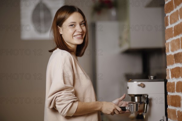 Woman smiling while using an espresso machine next to a brick wall