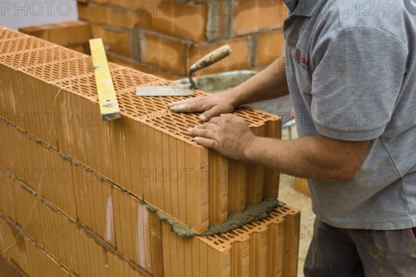 Anonymous construction worker on a building site erecting a brick wall. Brick wall of a solid house. Symbolic image for illegal labour and bungling