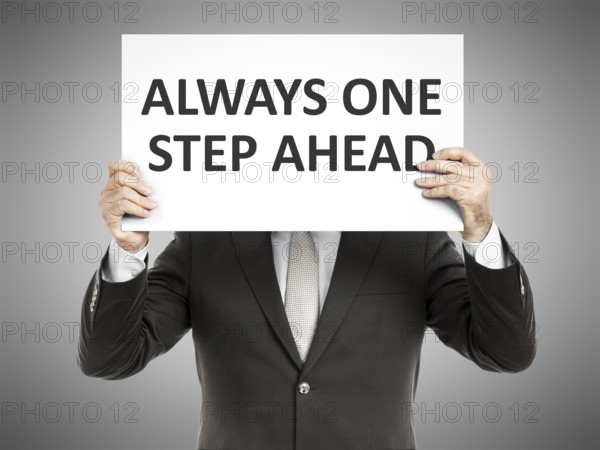A business man holding a paper in front of his face with the message always one step ahead