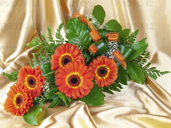 Bouquet of gerberas with green leaves over golden background