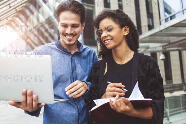 Two smiling colleagues are chatting in the street during lunch break near the building in the background