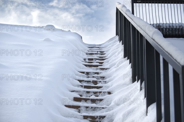 Winter scene where a set of stairs is almost completely covered in snow and railing on the right side of the stairs