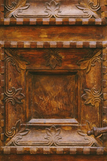 Close-up texture of brown wooden doors with raised carvings and square patterns.
