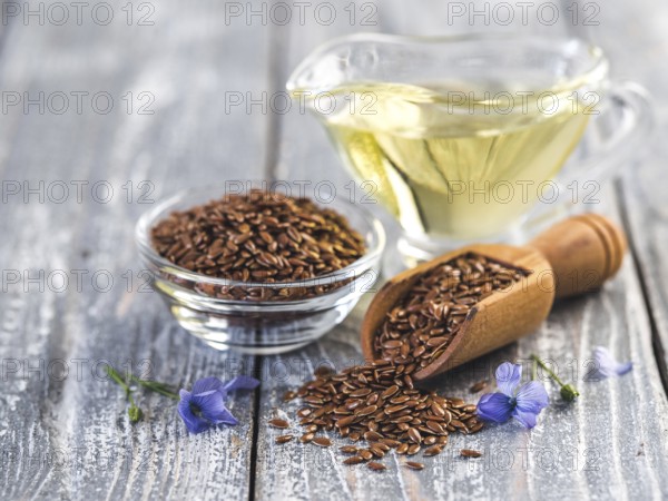 Flax seeds and flax oil. Brown linen seeds, flaxseed oil and blue flax flowers on old gray wooden background. Copy space