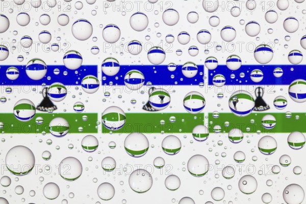 Flags of Lesotho behind a glass covered with raindrops. 3D illustration