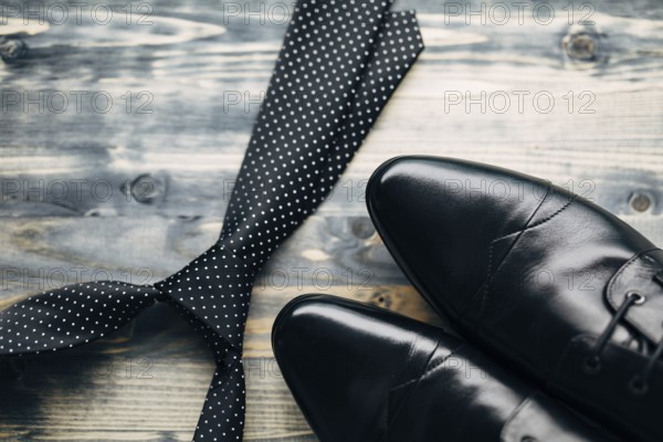 Black tie with white polka dots and men's leather shoes on a wooden background.