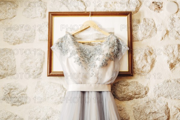 White wedding dress of the bride with patterns on a hanger on the picture frame.