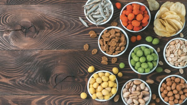 Assortment of different snack for beer, wine, party. Peanuts in coconut glaze, green vasabi, red spicy chilli, yellow cheese glaze, chips, pistachio, crackers, fish on brown wooden table. Copy space