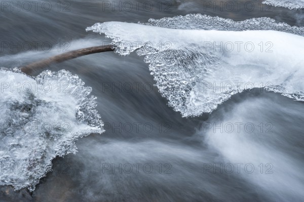 Long exposure in the current of a stream from a branch between two rocks covered with ice
