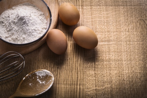 Three eggs flour in bowl empty spoon corolla on wooden board