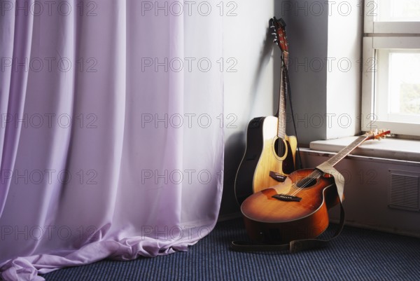 Two acoustic guitar next the window and drapery