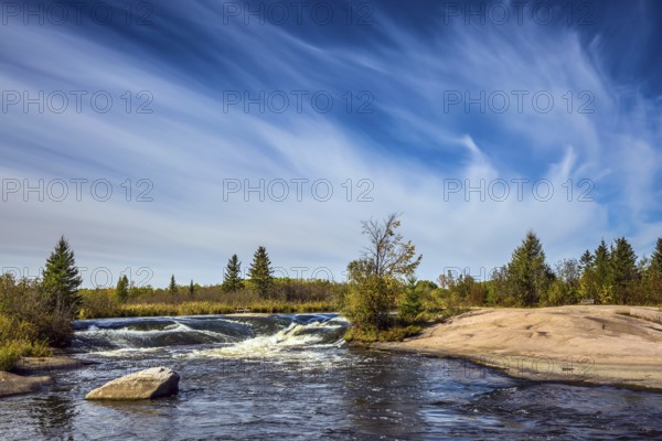 Foam water rapids on the smooth stones of the Winnipeg River. Thin cirrus clouds. Trend of travel Around the World. Old Pinawa Dam Provincial Heritage Park