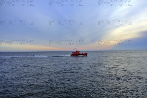 An orange-coloured pilot boat sails on the calm sea at sunrise under a blue sky, 27472 Cuxhaven, Germany, Europe