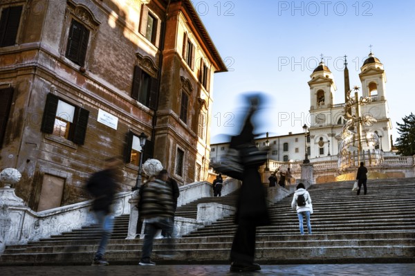 People in motion on the steps of the Spanish Steps in front of historic buildings under a blue sky, Rome
