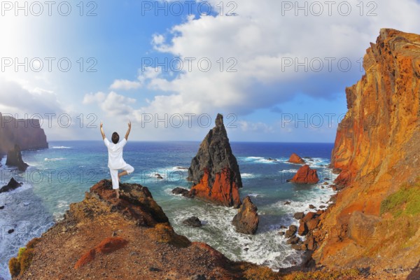 The woman ashore in a white suit for yoga carries out a pose Tree. Atlantic storms. Colorful pinnacles lit sunset. Arid eastern tip of the island of Madeira