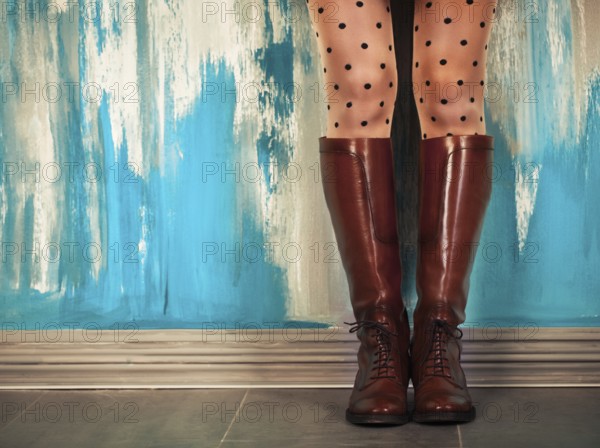Female legs in high brown leather boots near the wall