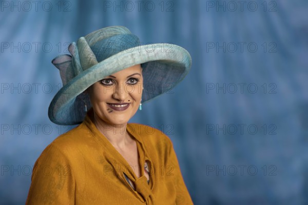 Woman wearing blue hat and yellow clothes, smiling in front of blue background, staged portrait shooting, studio shot, Mindelheim, Bavaria, Germany, Europe