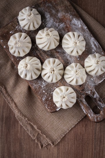 Freshly frozen khinkali, raw, on a wooden chopping board, top view, rustic style, no people