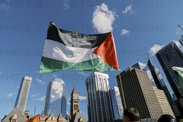 Toronto, Canada - 28 October 2023: Palestinian flag flies high amidst the city skyline, with skyscrapers and an old clock tower standing tall in the background.