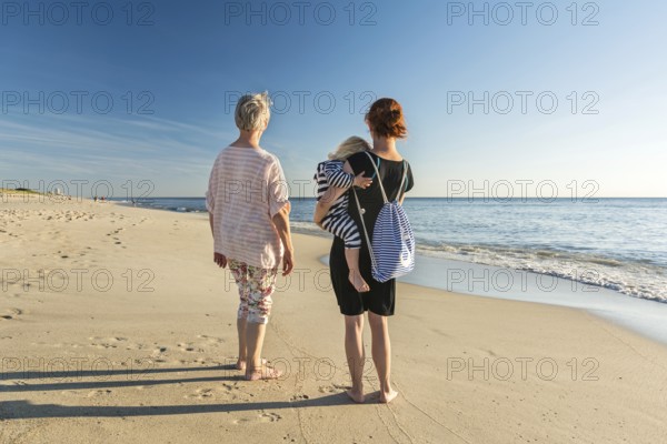 Young and old women standing at the beach in the evening sun looking towards the horizon