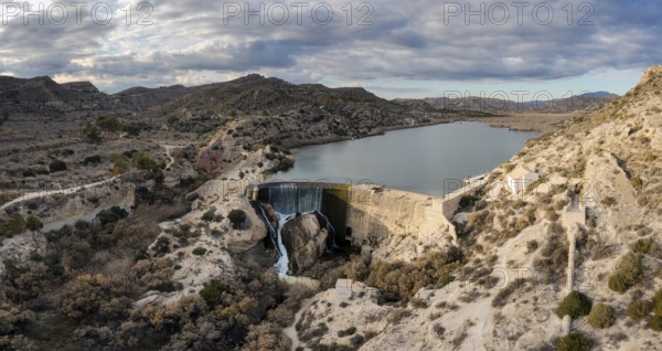 A drone view of the Elche Reservoir and dam wall with waterfall and surrounding semi-desert landscape