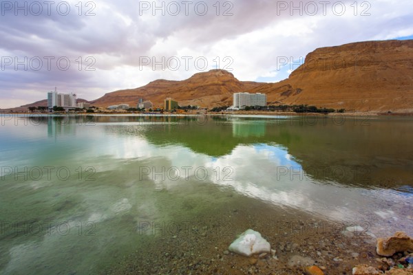 Quiet windless winter day. The smooth surface of the very salty sea water reflects the sky and clouds. Legendary Dead Sea. Israel