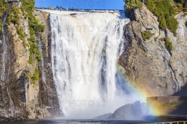 Magnificent rainbow in the spray of the waterfall Montmorency in Montmorency Falls Park. Above the waterfall built bridge for walking. The concept of active and cultural tourism